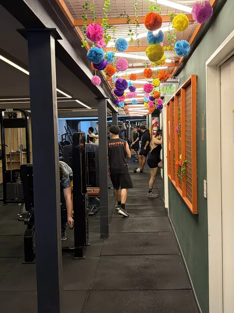 Pasillo de la sala con pompones de colores colgados del techo y socios entrenando entre las máquinas.