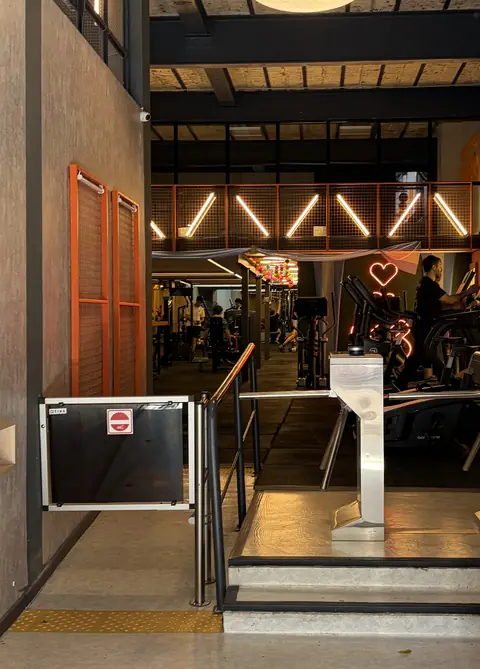La entrada al gimnasio: el molinete, las rejas naranjas y las luces de la sala al fondo.
