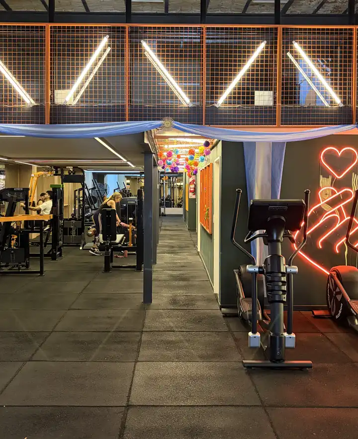 La sala de Pantera: tubos de luz en diagonal sobre rejas naranjas, máquinas de musculación, elípticas y un neón con forma de corazón.