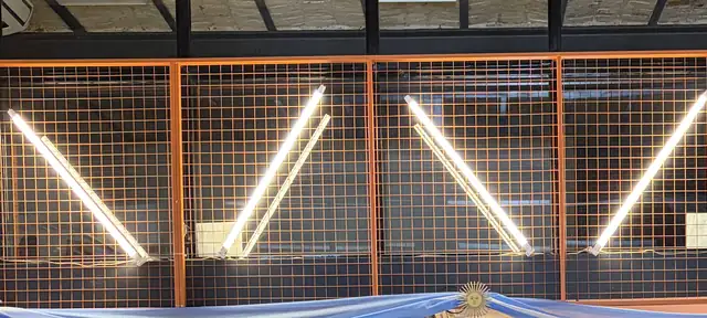 Tubos de luz blanca en diagonal sobre las rejas naranjas del entrepiso.